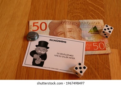 Stockholm, Sweden. May 02, 2021. 
One Monopoly Game Card Written In Swedish: Collect 50 M From Selling Shares. Real Money On A Wooden Background. Boardgame Pieces Surrounding The Banknotes. 