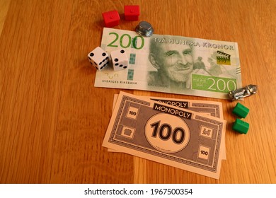 Stockholm, Sweden. May 02, 2021. Real Swedish Money Next To Monopoly Money On A Wooden Background. Boardgame Pieces Surrounding The Banknotes. Currency For 200 SEK. (Swedish Krona)