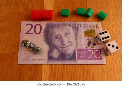 Stockholm, Sweden. May 02, 2021. Real Swedish Money Next To A Wooden Background. Monopoly  Boardgame Pieces Surrounding The Banknote. Currency For 20 SEK. (Swedish Krona)