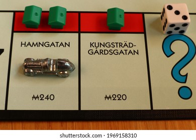 Stockholm, Sweden. May 02, 2021. Monopoly Board Game. Close Up Over The Red Streets Kungsträdgårdsgatan, Hamngatan. Written In Swedish. The Metal Car Token, Dice And Green Houses. Classical Boardgame.