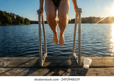 Stockholm, Sweden A woman's legs dangle from a bathing ladder on a lakeside dock in the summer sun. - Powered by Shutterstock