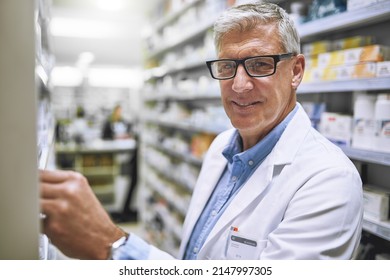 Stocking Up On Some New Meds. Portrait Of A Cheerful Mature Male Pharmacist Getting Medication From A Shelf While Looking At The Camera In A Pharmacy.