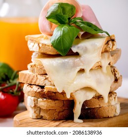 Stockpile of toasted melted cheese pressed sandwiches with ham meat, cherry tomatoes, orange juice and basil leaves on wooden cutting board. Close up. Square image - Powered by Shutterstock