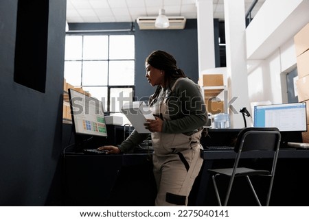 Stockroom employee checking merchandise logistics on computer, working at customers orders in warehouse. African american manager standing at counter desk preparing packages in storehouse