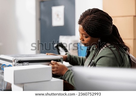 Stockroom supervisor looking at metallic box, checking product quality control before shipping to client. Warehouse worker standing at counter desk preparing packages in storage room