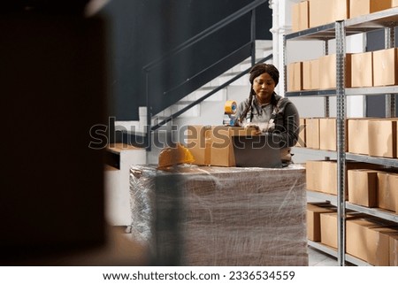 Stockroom worker preparing customers orders, using adhesive tape to pack products in cardboard boxes in warehouse. Storage room supervisor wearing industrial overall during storehouse inventory
