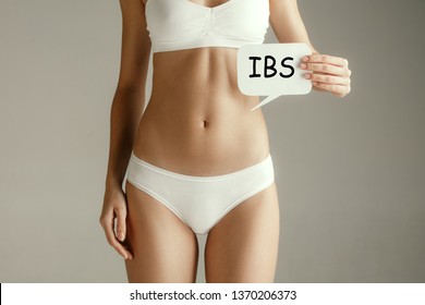 Stomach Ache Concept. The Woman With Text IBS On Gray Studio Background. Irritable Bowel Syndrome Or IBS Month Concepts