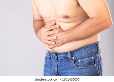 Stomach Ache Or Pain On Belly Concept : Fat Man Using His Hand And Pressing On Stomach On Grey Background