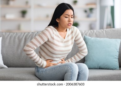 Stomach Ache. Sick Asian Woman Suffering From Acute Abdominal Pain At Home, Upset Korean Female Having Menstrual Pain Or Problems With Digestion, Sitting On Couch And Touching Belly, Free Space