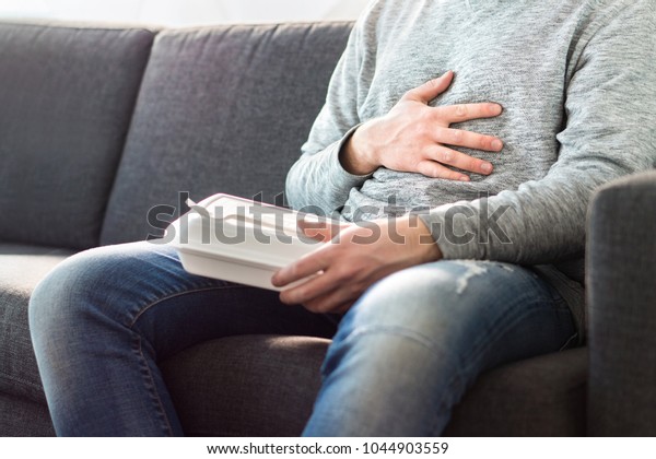 Stomach pain, food poisoning or\
digestion problem after fast junk food. Man ate too much and is\
holding belly with hand. Indigestion, heart burn or unhealthy\
diet.