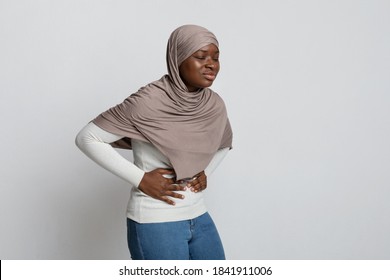 Stomach Pain. Sick African Muslim Woman In Hijab Suffering From Acute Abdominal Ache, Upset Black Islamic Lady Touching Belly, Feeling Unwell While Standing Over Light Studio Background, Copy Space