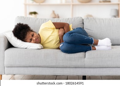 Stomachache. Black Teen Girl Suffering From Abdominal Pain Touching Aching Stomach Lying On Sofa At Home.