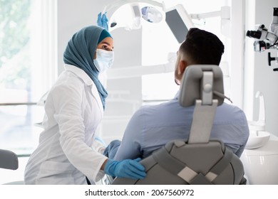 Stomatologic Check Up. Muslim Female Dentist Doctor Having Appointment With Male Patient In Modern Clinic, Islamic Stomatologist Woman Wearing Hijab And Protective Medical Mask, Closeup Shot