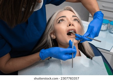 Stomatologist checkup. Close-up of a young woman with her mouth open, a dentist with the help of dental equipment makes an examination of the oral cavity - Powered by Shutterstock