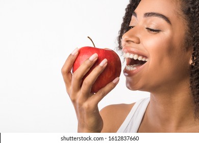 Stomatology Concept. African american woman eating red apple, showing healthy teeth. Copy space