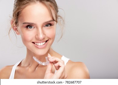 Stomatology Concept, Head And Shoulders Of Woman With Strong White Teeth Looking At Camera And Smiling, Holding False Tooth, Denture. Young Woman At Dentist's, Invisalign Orthodontics