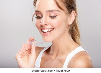 Stomatology Concept, Head And Shoulders Of Woman With Strong White Smiling, Holding False Tooth, Denture. Young Woman At Dentist's, Invisalign Orthodontics, Studio, Indoors