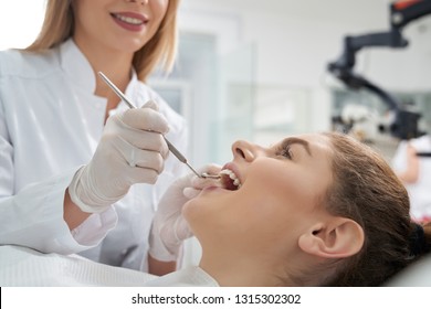 Stomatology doctor treating woman's teeth in dentistry clinic. Happy woman lying with opened mouth. Female dentist in white uniform and gloves using restoration instruments.