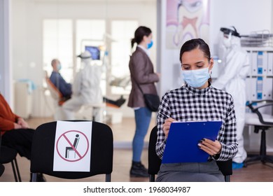 Stomatology Patient In Denstiry Wainting Area Filling Form Before Consultation With Dentist Dressed In Ppe Suit As Safety Precation Agasint Infection With Coronavirus ,during Global Outbreak.