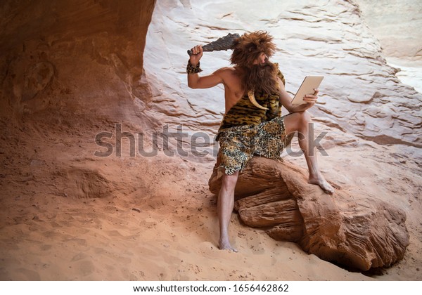 Stone Age luddite caveman scratching his head with a
club while looking at his stone tablet outdoors in a weathered rock
cave