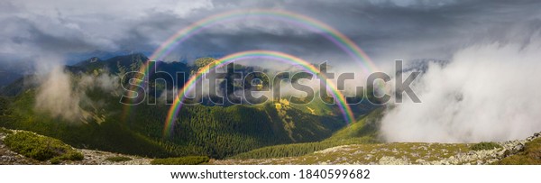 The stone\
Alps mountains are beautiful with a toothy panorama of mountain\
peaks. Panorama of stone wasteland amid thunderclouds and fog .\
Beautiful double rainbow above the\
fog