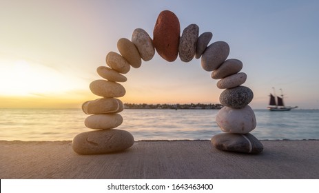 Stone arch with a red stone at the top, at sunset on a beach. Mediate, balance and stability Concept.