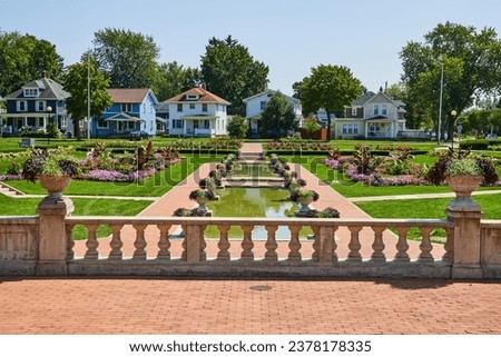 Stone balcony with brick path and pools of water surrounded by flower beds and distant houses