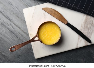 Stone board with saucepan of clarified butter and knife on table, flat lay