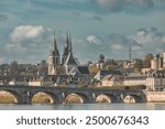 A stone bridge arches over the Loire River in Tours, France, with the iconic twin spires of the Saint-Martin Basilica rising above the town