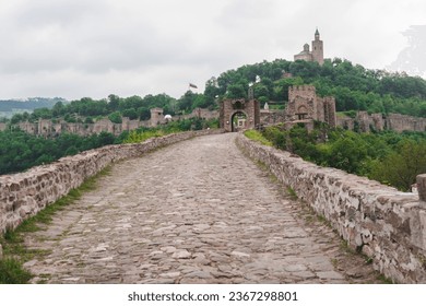 A stone bridge leads to an ancient castle on a green hill. Panorama of the old Bulgarian medieval fortress. A beautiful view of the historical place. Concept of tourism and travel. - Powered by Shutterstock