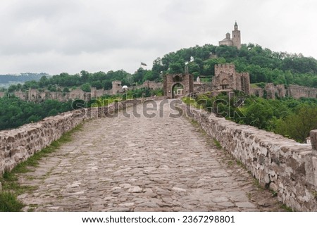 A stone bridge leads to an ancient castle on a green hill. Panorama of the old Bulgarian medieval fortress. A beautiful view of the historical place. Concept of tourism and travel.