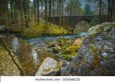 Stone bridge at the river spring of Kamniska Bistrica in Slovenia in dry winter time. Cold enchanted bridge with flowing water underneath in the middle of the forest.