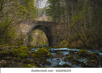 Stone bridge at the river spring of Kamniska Bistrica in Slovenia in dry winter time. Cold enchanted bridge with flowing water underneath in the middle of the forest.