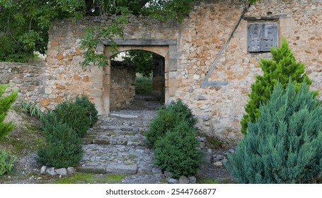 A stone building with a stone archway and a stone staircase leading up to it. The building is surrounded by bushes and trees - Powered by Shutterstock