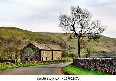 A Stone Built Barn And Solitary Tree At The Side Of A Country Lane In The Yorkshire Dales, England, Set Again A Backdrop Of Fells