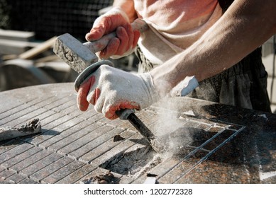 Stone carver in gloves working with a hammer and chisel on a marble slab. heavy handwork. production of monuments from marble. working with natural stone