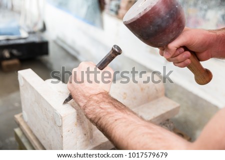 Stone carver working with hammer and chisel at marble column