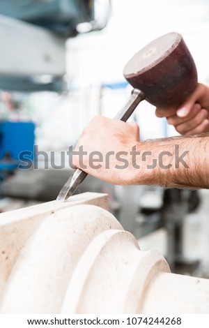 Stone carver working with hammer and chisel at marble column