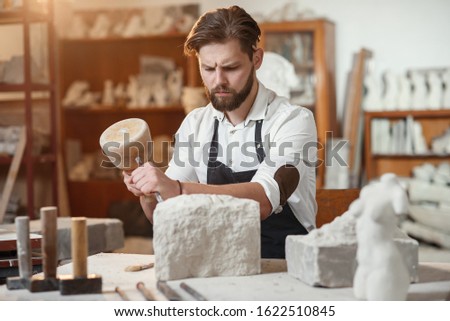 Stone carver works with wooden hammer and chisel at limestone.