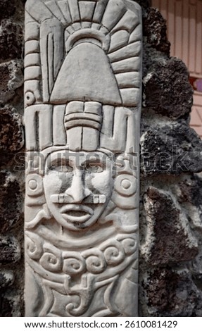 A stone carving of a man with a bird on his head. The carving is of a Mayan figure and is made of stone
