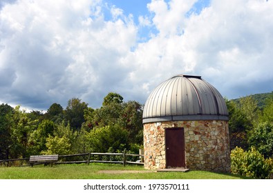 Stone, Circular Building Houses The Bays Mountain Observatory, In Bays Mountain State Park.  Wooden Fence Runs Besides It.  Wooden Park Bench Sits Solitary Besides Structure.