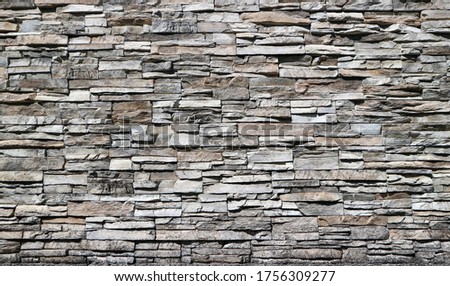 Stone cladding wall made of striped stacked bricks of natural brown and gray rocks .
