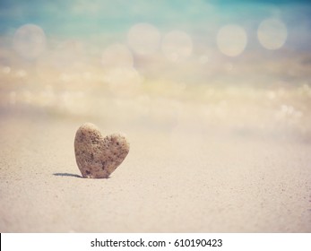 Stone heart shape standing on summer beach sand, love concept.