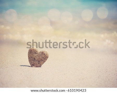 Stone heart shape standing on summer beach sand, love concept.