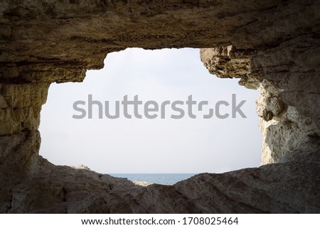 	
Stone hole entrance or opening in rock cave wall looking at sky and sea