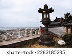 Stone lantern antique korean style and small buddha statue on viewpoint in Sanbangsa Temple with view landscacpe Jeju island and cityscape Seogwipo city urban in Jeju do capital of South Korea