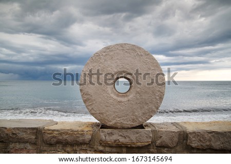 Stone millstone on the embankment of the Adriatic Sea against the backdrop of a stormy sea, Montenegro.