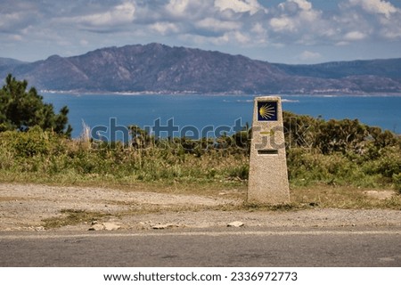 Stone monolith that marks the direction to follow for the road to Santiago, with arrow and shell, with the ocean in the background. Concept pilgrim, way, religion, travel.