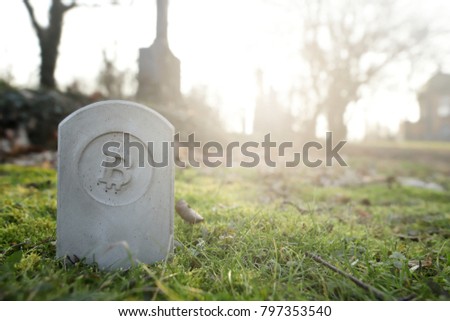 stone monument/tombstone with bitcoin symbol standing in green grass on cementery - wide angle view - sunny blurred background with space for text - economic/financial concept