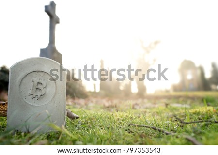 stone monument/tombstone with bitcoin symbol standing in green grass on cementery in front of stone cross - wide angle view - sunny blurred background with space for text - economic/financial concept